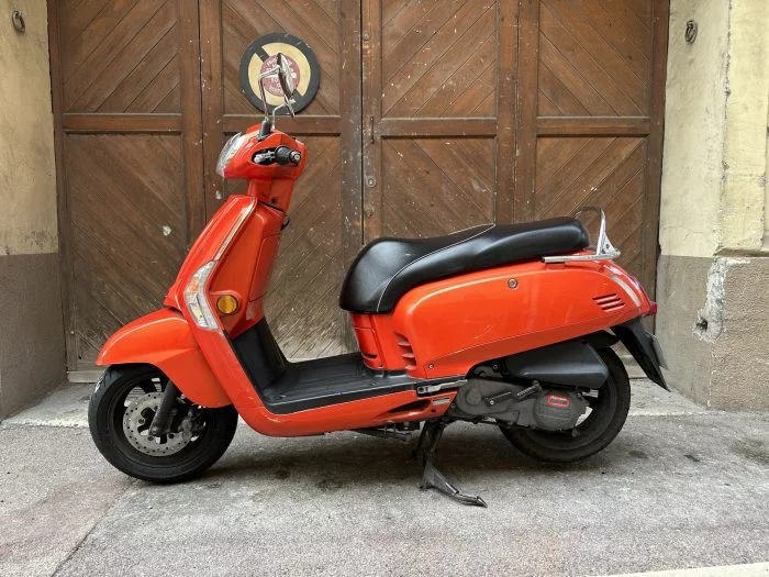 Scooter orange photographié devant une porte en bois